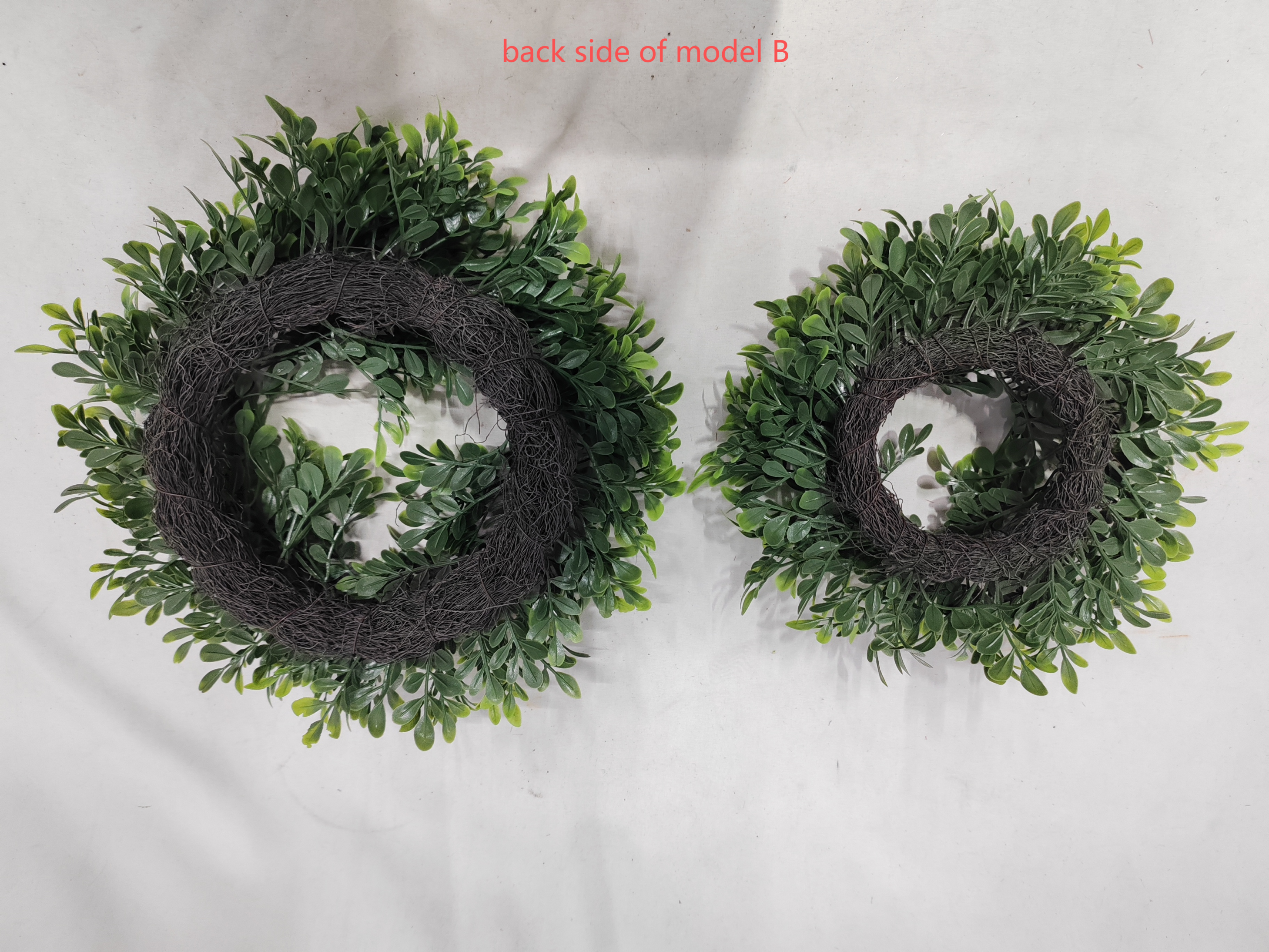 Two artificial boxwood wreaths, large and small, showing the back with dark twig bases and green foliage on a light surface; text reads 'back side of model B'.