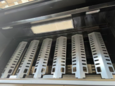 Interior of a gas grill showing six perforated heat plates under the lid and a rectangular ceramic panel at the back.