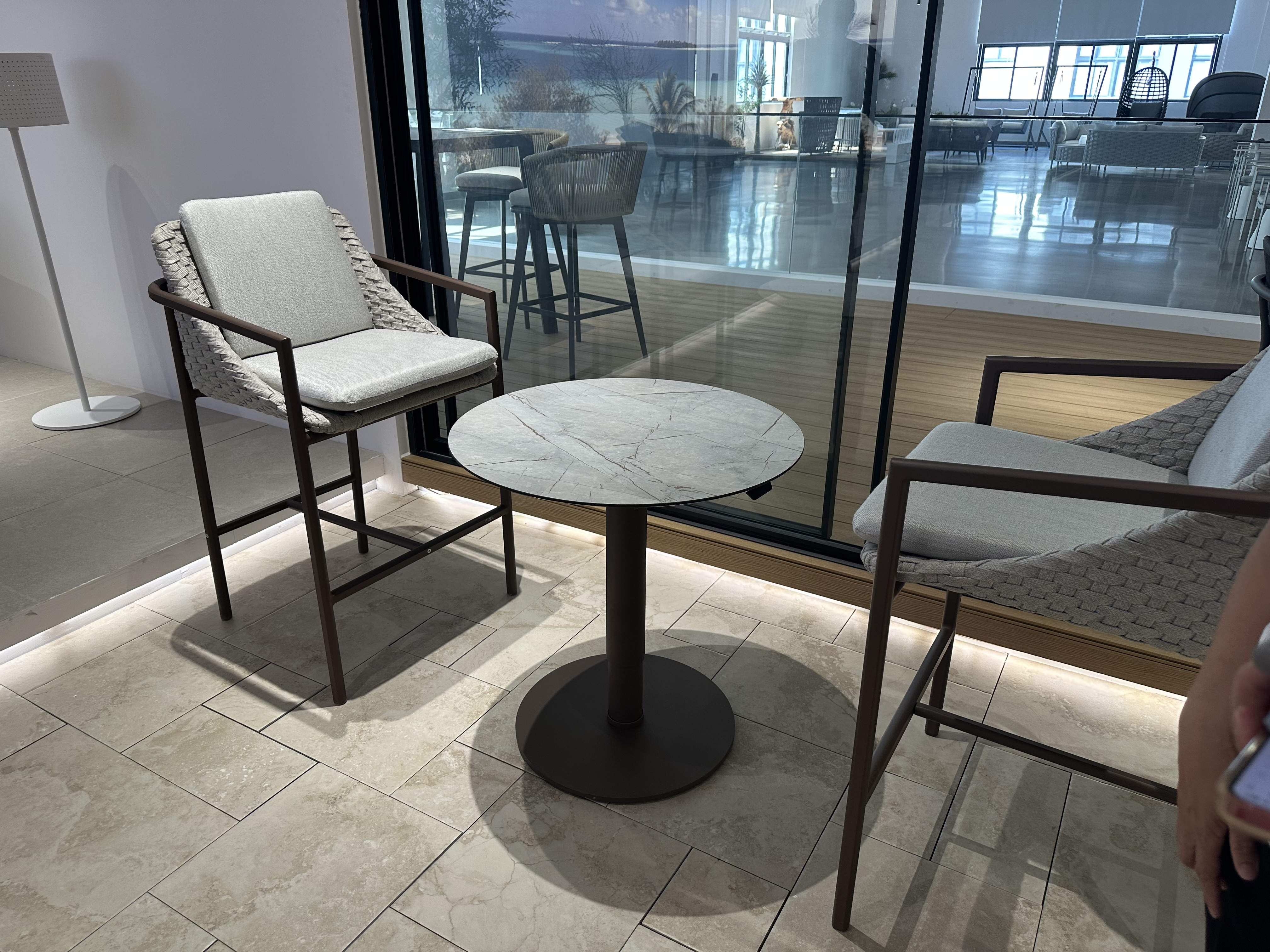 Two cushioned patio chairs with braided backs around a small round marble-look table beside a glass partition.